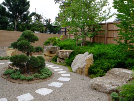 Garten mit Steinen, Bäumen und einem geschwungenen Kiesweg.