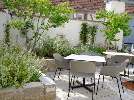 Garten mit Blumen, Bäumen und modernen Tischen und Stühlen.